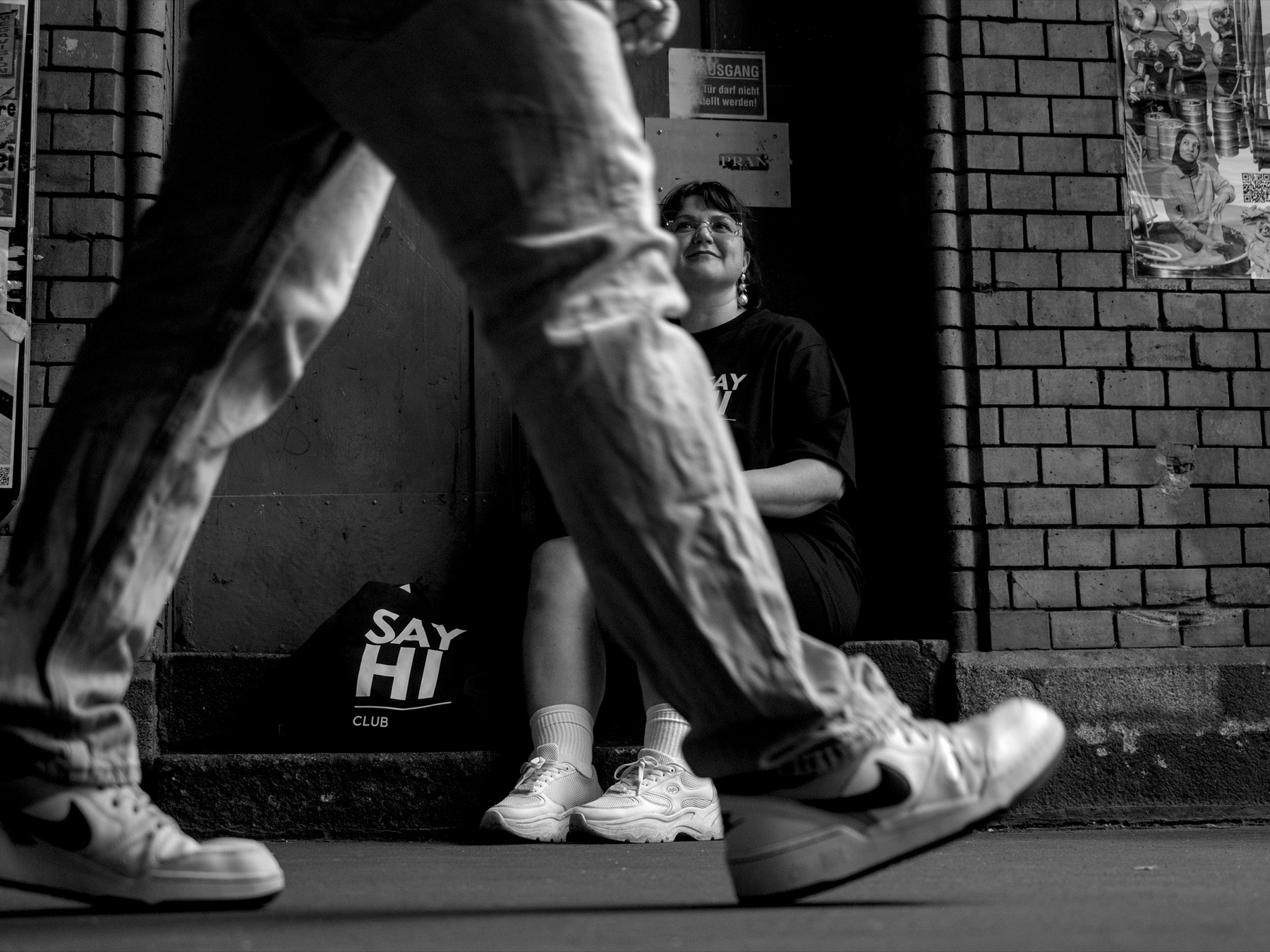 A woman smiling up at someone walking past, SAY HI Club tote bag on the ground